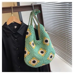 Detail van een handgebreide muntgroene schoudertas met gele zonnebloempatronen erop