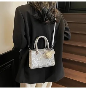 Silver snakeskin bag with woven handle and pearl bow charm shown with black suit