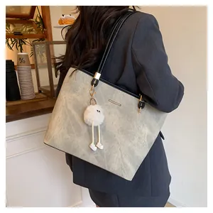 Detailed side view of a large light grey tote bag with thin black straps and plush charm