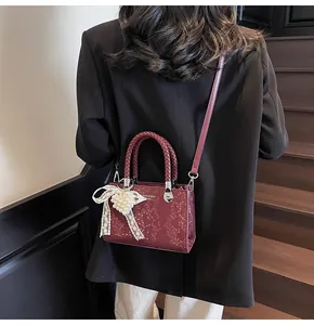 Close-up of burgundy snake-embossed handbag with woven handle and heart pendant accessory