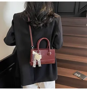 Detail of burgundy glossy leather handbag with pearl heart charm and lace bow decor