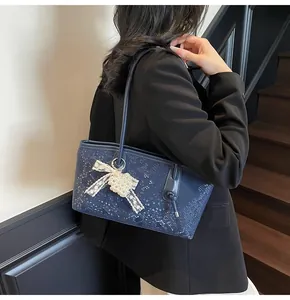 Detail of navy blue snakeskin texture shoulder bag with white lace bow and pearl heart charm