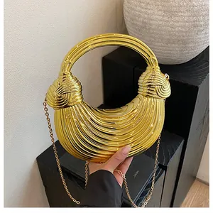 Macro shot of gold crescent metal handbag featuring twisted knot handle and chain strap