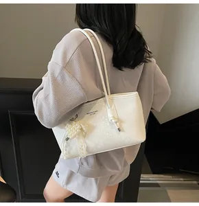Detail of white snakeskin texture tote bag featuring pearl heart charm and brand logo
