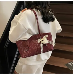 Detail of burgundy snakeskin shoulder bag with lace bow and pearl charm worn on shoulder