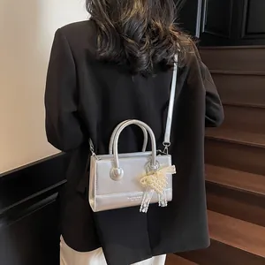 Silver square crossbody bag with pearl bow pendant shown on a model in black blazer