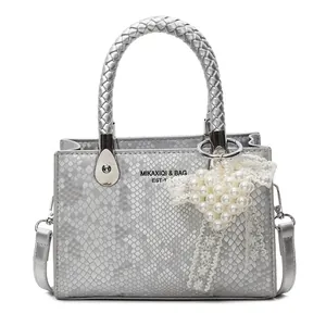 Silver snakeskin tote bag with woven handle and pearl lace heart charm on white background
