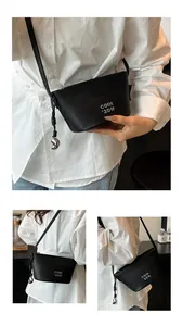 Détails du sac bandoulière en cuir grainé noir avec logo argenté et pendentif fève