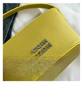 Détail de la texture cuir jaune grainé et du logo métallique argenté sur le sac à main