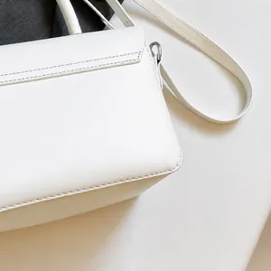 Close-up of premium white faux leather shoulder bag with fine stitching and metal hooks