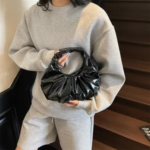 Borsa a mano plissettata nera lucida indossata da una modella su una scala in legno