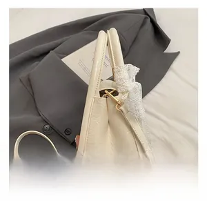 Close-up of cream textured leather bag featuring a gold hook and white lace bow detail