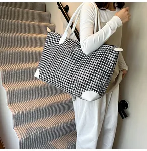 Model showing large black and white houndstooth travel bag on a modern staircase