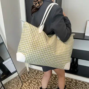 Large green and white houndstooth travel bag with white leather handles worn by model
