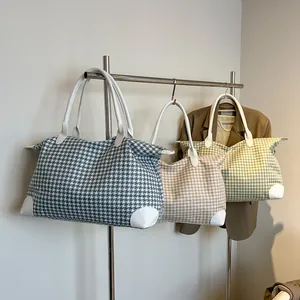Three houndstooth travel tote bags in blue, khaki, and green hanging on a metal rack