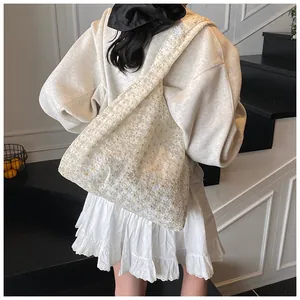 Detail of floral lace embroidery on cream mesh tote bag worn by model in light setting