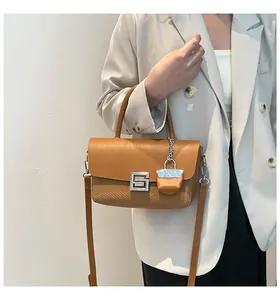 Close-up of brown textured crossbody bag with silver G-buckle and mini pouch detail