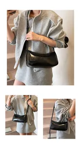 Close-up of black glossy underarm bag with adjustable strap and sleek crescent design