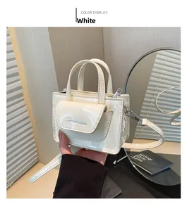 Detail einer kleinen weißen Lacklederhandtasche mit Glanzeffekt und silbernem Textdekor
