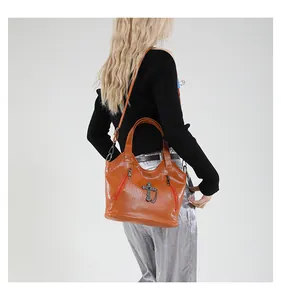 Detail of a shiny brown leather handbag with a vintage metal cross and side zippers
