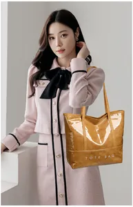 Mustard yellow patent leather tote bag with white TOTE BAG text carried by a model