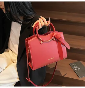 Détail du sac cabas en cuir rouge avec logo doré et poignées rondes métalliques