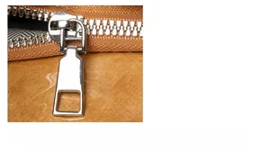 Detailed macro view of smooth silver metal zipper pull on a vintage brown tote bag