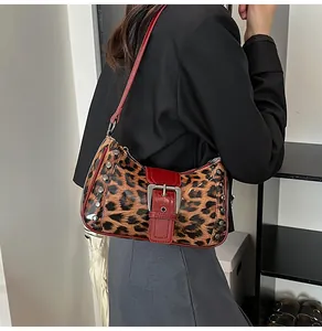Detail of leopard print shoulder bag with silver studs and red buckle strap on a model