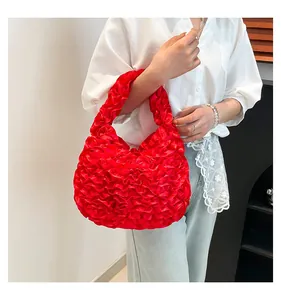 Detail of red pleated satin handbag with ruffled design held by a model in casual outfit