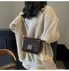 Close-up of a dark brown glossy shoulder bag with a rectangular silver metal buckle detail