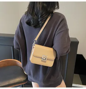 Close-up of khaki square crossbody bag with silver buckle worn over purple top