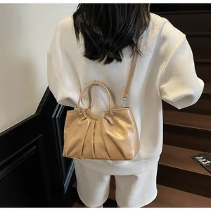 Detail of light brown pleated crossbody bag with cylinder handles and silver hardware