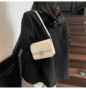 Detail of a minimalist ivory shoulder bag with glossy finish and silver buckle on a model