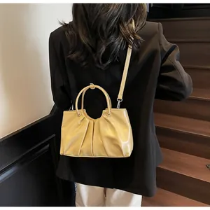 Close-up of pleated pale yellow bucket bag with slender strap on a wooden staircase