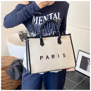 Detail of a beige canvas tote bag with black PARIS print and leather straps