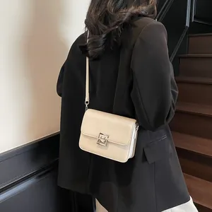 Minimalist cream white square crossbody bag with metallic clasp on a leather surface