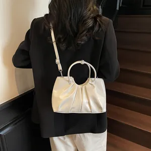 Minimalist white pleated bucket bag with round metal handle and adjustable crossbody strap