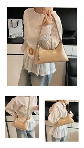 Detail of a beige half-moon hobo bag in glossy PU leather with silver metal pendant