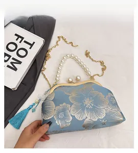 Detail of blue brocade clutch featuring floral gold embroidery and pearl handle