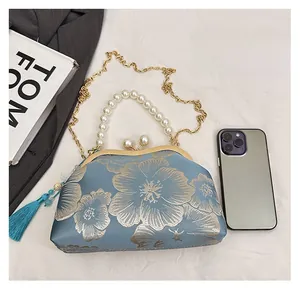 Detailed comparison of embroidered ethnic handbag size next to a phone and book