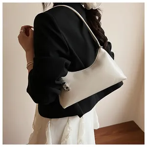 White crescent PU leather bag with silver metal pendant shown on shoulder in a minimalist setting