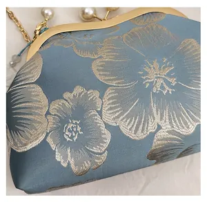 Detailed embroidery texture on vintage blue clutch with golden frame and pearl clasp