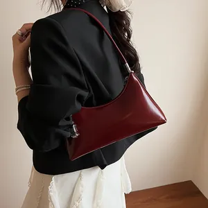 Deep red crescent underarm shoulder bag in glossy leather worn with a blazer