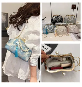 Detail of embroidered floral handbag featuring pearl handle and metallic frame clasp