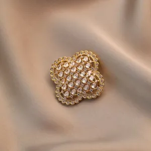 Gouden klavervier broche met zirkonen op een champagnekleurige zijden achtergrond