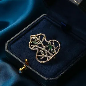 Hollow gourd brooch with gold frame, white zircons and green gems on dark velvet