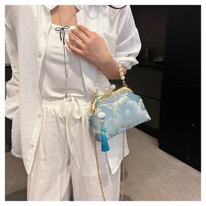Macro detail of blue satin bag with gold floral embroidery, pearl clasp, and blue tassels