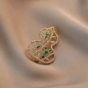 Broche de calabaza dorada hueca con circonitas blancas y gemas verdes sobre seda