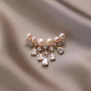 Elegante Goldbrosche mit Naturperlen und Zirkonia-Quasten auf Champagner-Seide