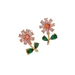 Elegantes pendientes de flor dorados con pétalos rosas y hojas verdes sobre fondo blanco